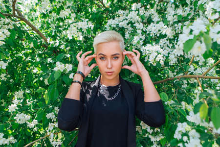 Young stylish business woman with short hair and nose piercing. Confident girl look like lesbian standing near the blooming apple treeの写真素材