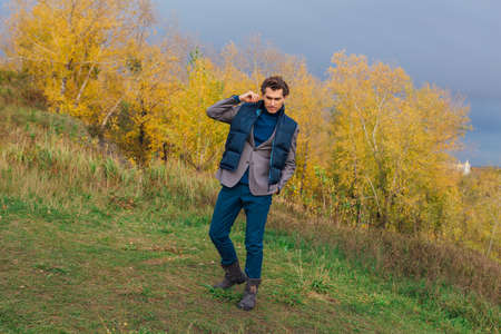 Tall handsome man walking outdoor in yellow autumn forest on the hill before stormの写真素材