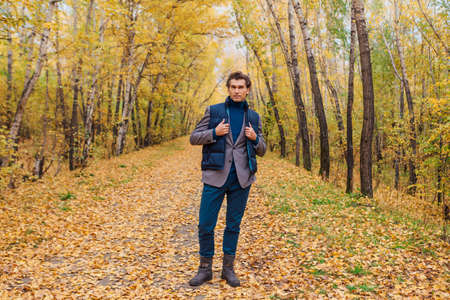 Tall handsome man dressed in a brown jacket walking in the autumn alleyの写真素材