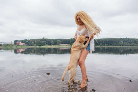 Young beautiful woman with blond curly hair playing with her labrador retriever dog in river.の写真素材