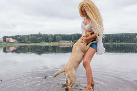 Young beautiful woman with blond curly hair playing with her labrador retriever dog in river.の写真素材