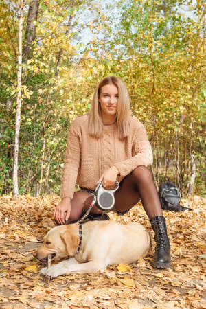 Young beautigul caucasian woman walking with her beloved labrador dog in autumn park with fallen golden leaves on the ground.の写真素材