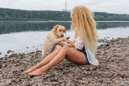 Young woman sitting with her labrador retriever dog on the river shoreの写真素材