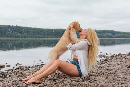 Young woman sitting with her labrador retriever dog on the river shoreの写真素材