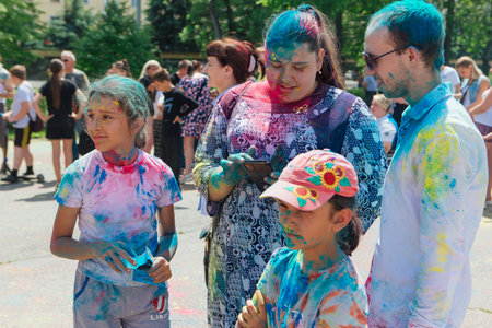 Novokuznetsk, Kemerovo region, Russia - June 12, 2022 :: Happy family with colorful faces painted with holi powder having fun outdoors.のeditorial素材