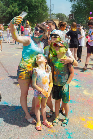 Novokuznetsk, Kemerovo region, Russia - June 12, 2022 :: Happy family with colorful faces painted with holi powder having fun outdoors.のeditorial素材