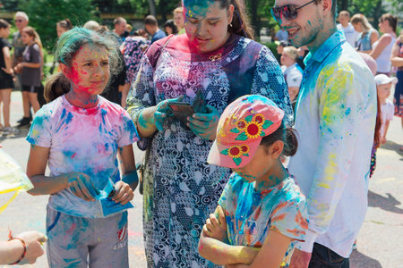 Novokuznetsk, Kemerovo region, Russia - June 12, 2022 :: Happy family with colorful faces painted with holi powder having fun outdoors.のeditorial素材