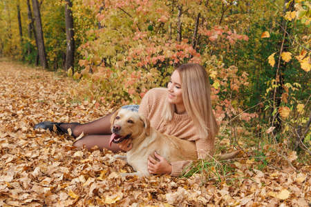 A young woman laying on the dry yellow leaves with her beloved labrador dog in autumn park.の写真素材