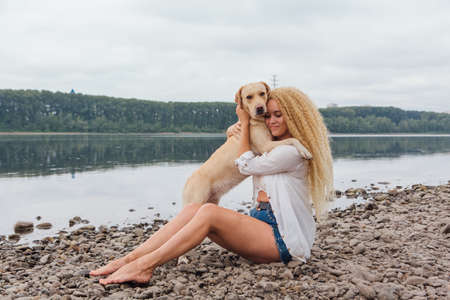 Young woman sitting with her labrador retriever dog on the river shoreの写真素材