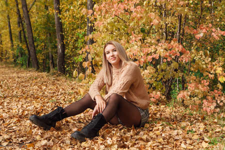 A beautiful young woman sitting in a forest on a dry autumn leaves.の写真素材