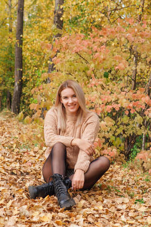 A beautiful young woman sitting in a forest on a dry autumn leaves.の写真素材