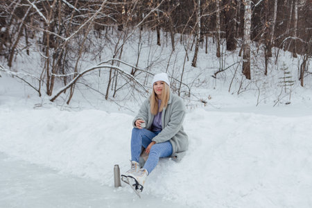 Lovely young woman relaxing after riding ice skates and drinking hot drink from thermo pot on the ice rink.の写真素材