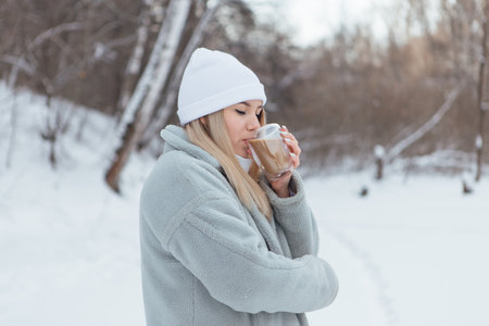 A beautiful young girl smiling and enjoying drinking coffee in a winter forest.の写真素材