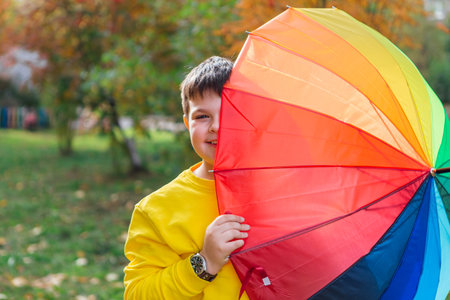 Cute boy under a colorful umbrella in autumn park.の写真素材