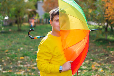 Cute boy dressed in yellow long sleeve standing under a colorful umbrella. A child in the autumn park posing with a rainbow umbrella.の写真素材