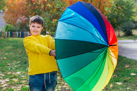 Cute boy dressed in yellow long sleeve standing under a colorful umbrella. A child in the autumn park posing with a rainbow umbrella.の写真素材