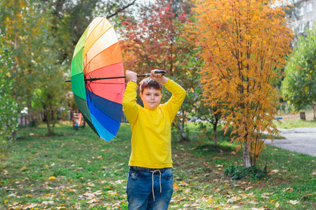 Cute boy dressed in yellow long sleeve standing under a colorful umbrella. A child in the autumn park posing with a rainbow umbrella.の写真素材