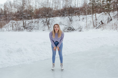Lovely young woman riding ice skates on the ice rink. Girl skating on ice in a winter frosty dayの写真素材