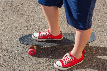Close up of feet of a boy in red sneakers rides on black penny skate board with pink wheels. Urban scene, city life. Sport, fitness lifestyle.の写真素材