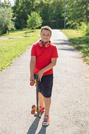 Chubby ten years old boy spends free time training skating in the city park. Cute nice boy enjoys sunny day outdoors with skateboard.の写真素材