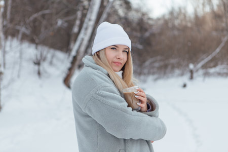 A beautiful young girl smiling and enjoying drinking coffee in a snowy winter forestの写真素材