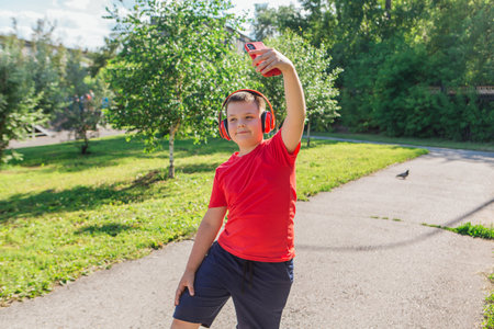 Happy chubby ten years old boy with headphones outdoors. Boy making selfie.の写真素材
