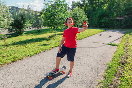 Chubby ten years old boy spends free time training skating in the city park. Boy looking on mobile phone.の写真素材