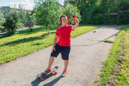 Chubby ten years old boy spends free time training skating in the city park. Boy looking on mobile phone.の写真素材