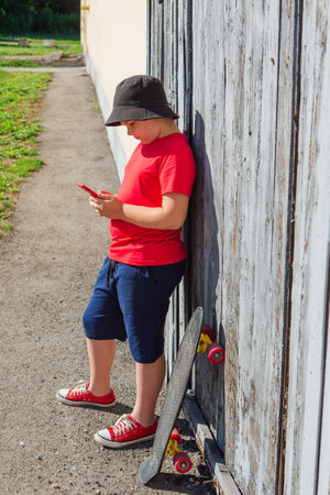Boy with plastic skateboard stars at the phone at hot summer day.の写真素材