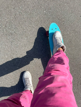 Close up of feet of a girl in white sneakers rides on blue plastic skate board with pink wheels. Urban scene, city life. Sport, fitness lifestyle.の写真素材