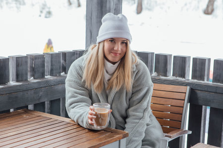 A beautiful young girl smiling and enjoying drinking coffee outdoors in a winter day.の写真素材
