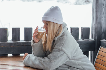 A beautiful young girl smiling and enjoying drinking coffee outdoors in a winter day.の写真素材