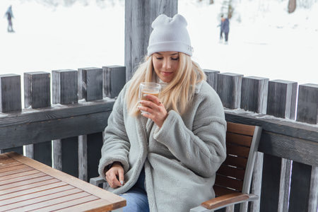 A beautiful young girl smiling and enjoying drinking coffee outdoors in a winter day.の写真素材