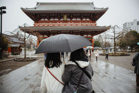 Sensoji Temple - Tokyo, Japan - February 16, 2020: 2 Asian women stay looking in front of Sensoji Temple and holding 1 black umbrella due rainy in the morning.のeditorial素材