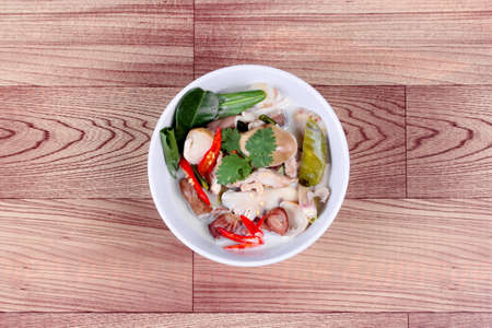 Chicken and galangal in coconut milk soup and herb on wood. Top view