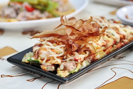 Close up Japan pizza as "Okonomiyaki" is fried mixed vegetable flour with meat topped sweet sauce ,mayonnaise or salad cream and sliced dried yellowfin tuna served with side dish. Selective focus.の写真素材