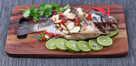Tilapia fish streamed with lemon topped spicy sour ginger and chili on butcher served. (Call Pla Nil Nuang Manoaw in Thai) isolated black background.の写真素材