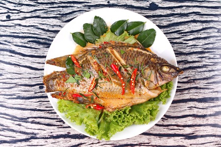 Curry-fried Tilapia fish with spicy topping on white dish.の写真素材