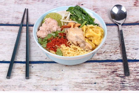 Boiled noodle and wonton in spicy sour soup as tom yum topped minced pork,chicken drumstick,chili,bean sprouts,cashew nut,Chinese mustard green and green lemon ,and chopsticksの写真素材
