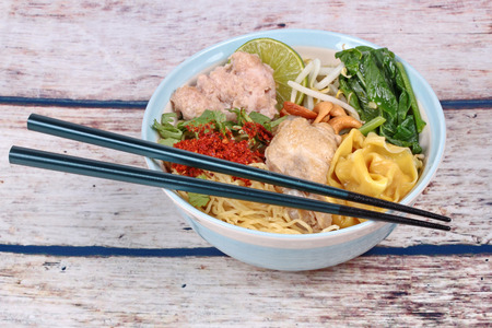 Boiled noodle and wonton in spicy sour soup as tom yum topped minced pork,chicken drumstick,chili,bean sprouts,cashew nut,Chinese mustard green and green lemon ,and chopsticksの写真素材