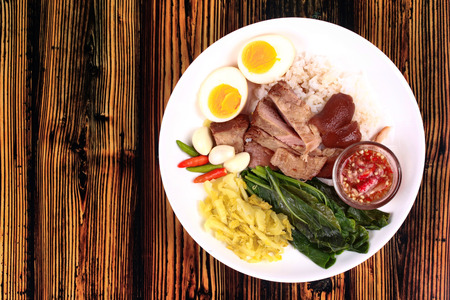 Chinese Thai food,Jasmine rice with stewed pork hock topped boiled eggs,boiled kale,chili,big garlic and pickled turnip with spicy sour sauce.Call Khao Kha Moo Palo in Thai. Have text space on left.の写真素材