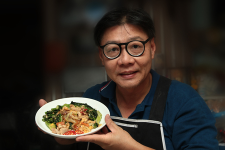 Thai Chinese food ,Chef holding a plate of fried big noodle with marinated chicken in soy sauce and vegetable call Sen Yai Pad Cee Oue in Thai.の写真素材