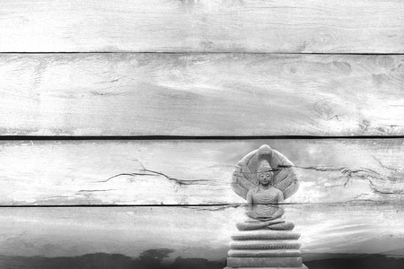 Black and white view ,Overlay the outdoor beautiful stone Buddha Image covered with seven heads of Naka (Great Snake) on Told wood texture.の写真素材
