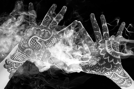 Black and white of the hands together to show the beautiful Henna tattoo at the open hands and arms with smoke and lightの写真素材