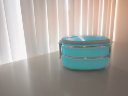 Blue  two-layer lunchbox of rice  is placed on a gray steel cabinet front window with a sunshade...