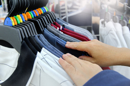 Using hand to choose a set of clothes wear by colour and size from  the  hanging display products.