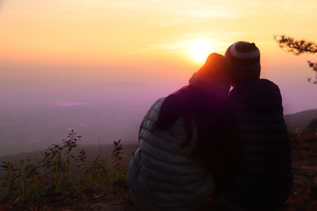 Silhouette image of men and women closer together. Sitting on the hillsides to scenic sky in the...