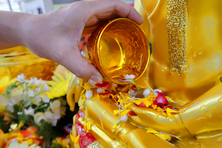 Pour some water with refreshing and colorful flower in metallic gold bowl on the hand of golden Buddha image to worship in the Songkran Festival.