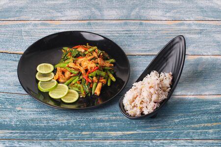 Thai cuisine , Spicy fried cowpea and basil with pork topped sliced green lemon served with japanese seed for rice in jasmine rice on black platesの写真素材