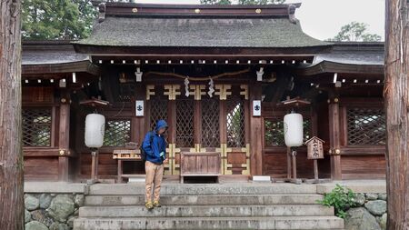 Wakayama City, Japan -14 July 2019: Tourist Backpacker teen is standing and protecting  body and  DSLR camera in front of Buddhist building of  Itakiso Jinja Shrine.のeditorial素材